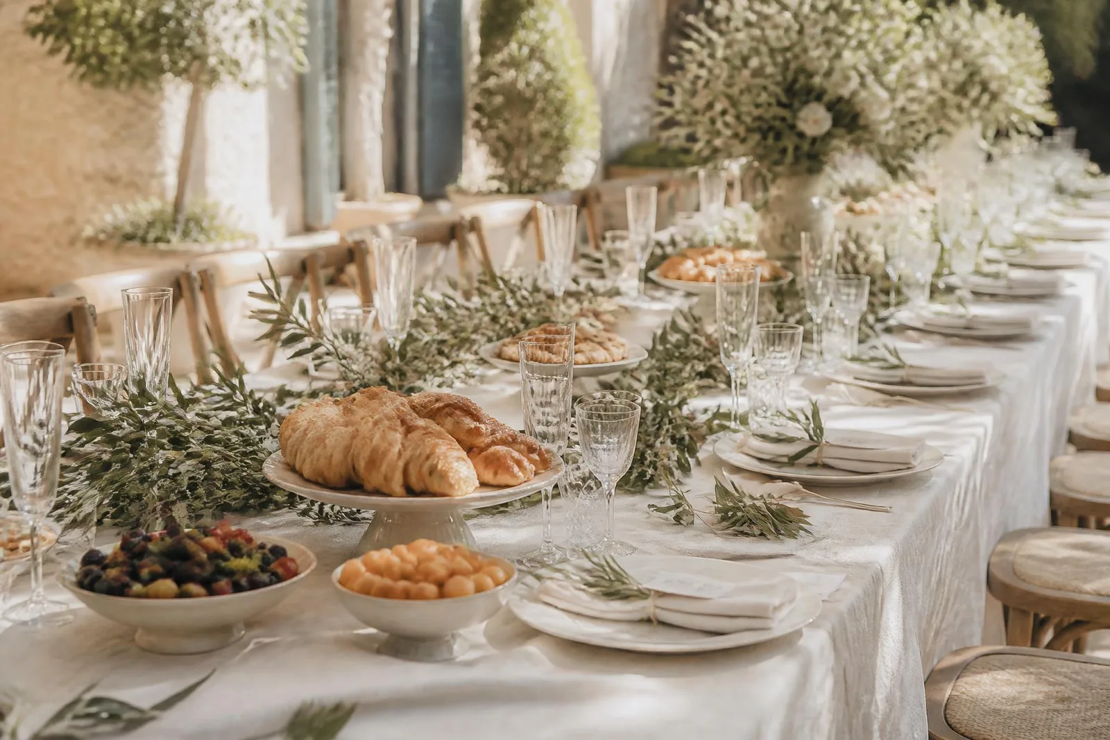 Table de brunch de mariage dressée en extérieur avec viennoiseries et branches d'olivier